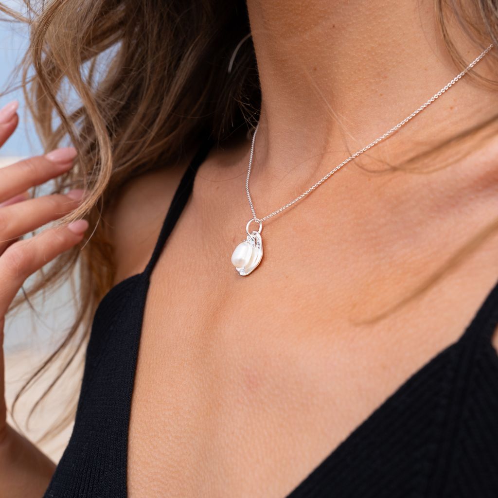 Close-up of a woman wearing a silver and pearl pendant.