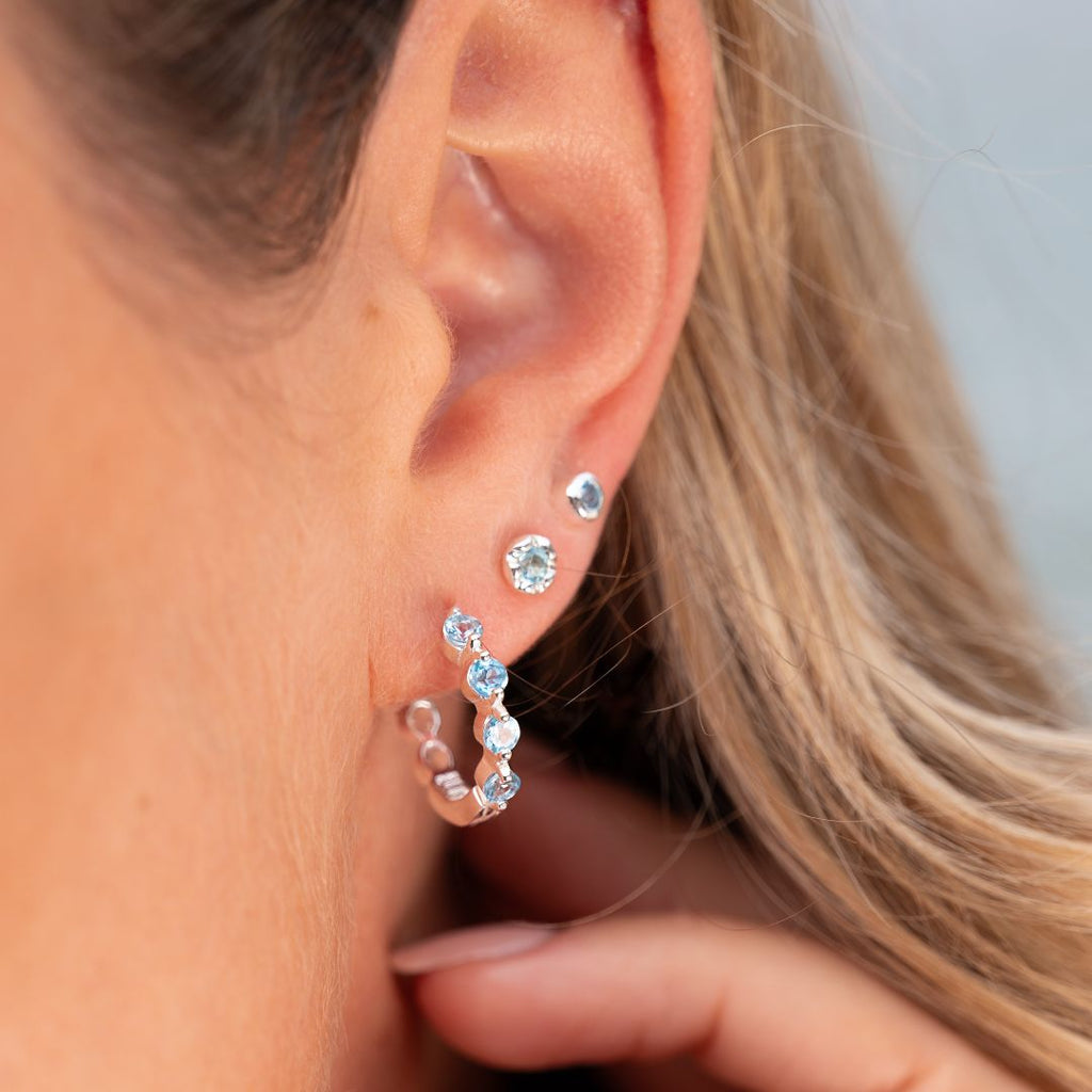 Close-up of an ear wearing blue topaz hoop, styled with two studs.