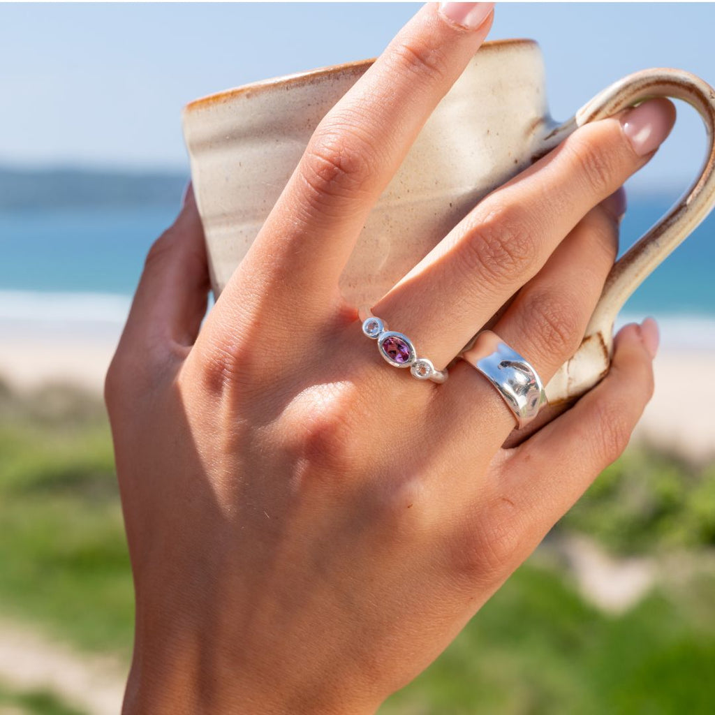 Hand holding a ceramic cup with pink tourmaline ring on finger.