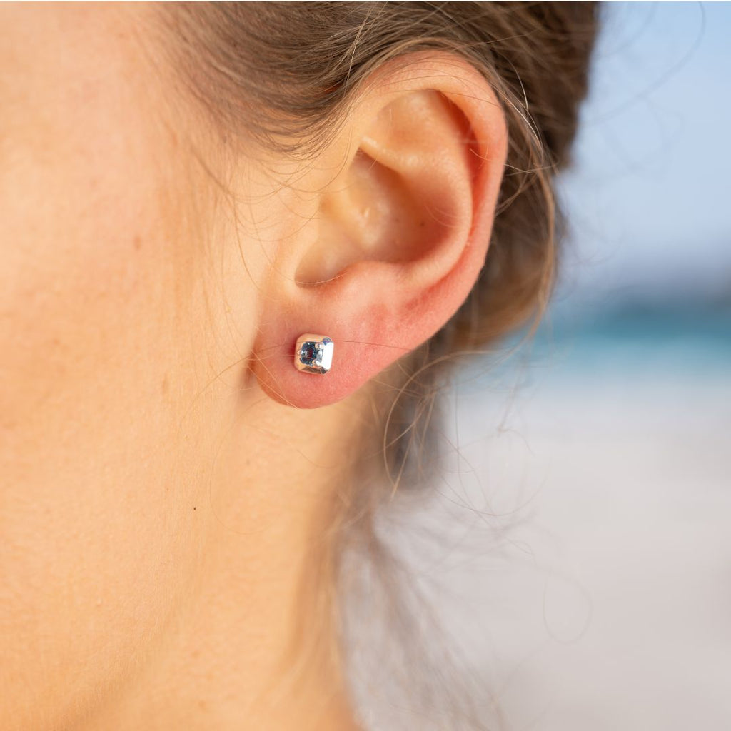 Close-up of an ear wearing a silver stud earring with a deep blue gemstone.