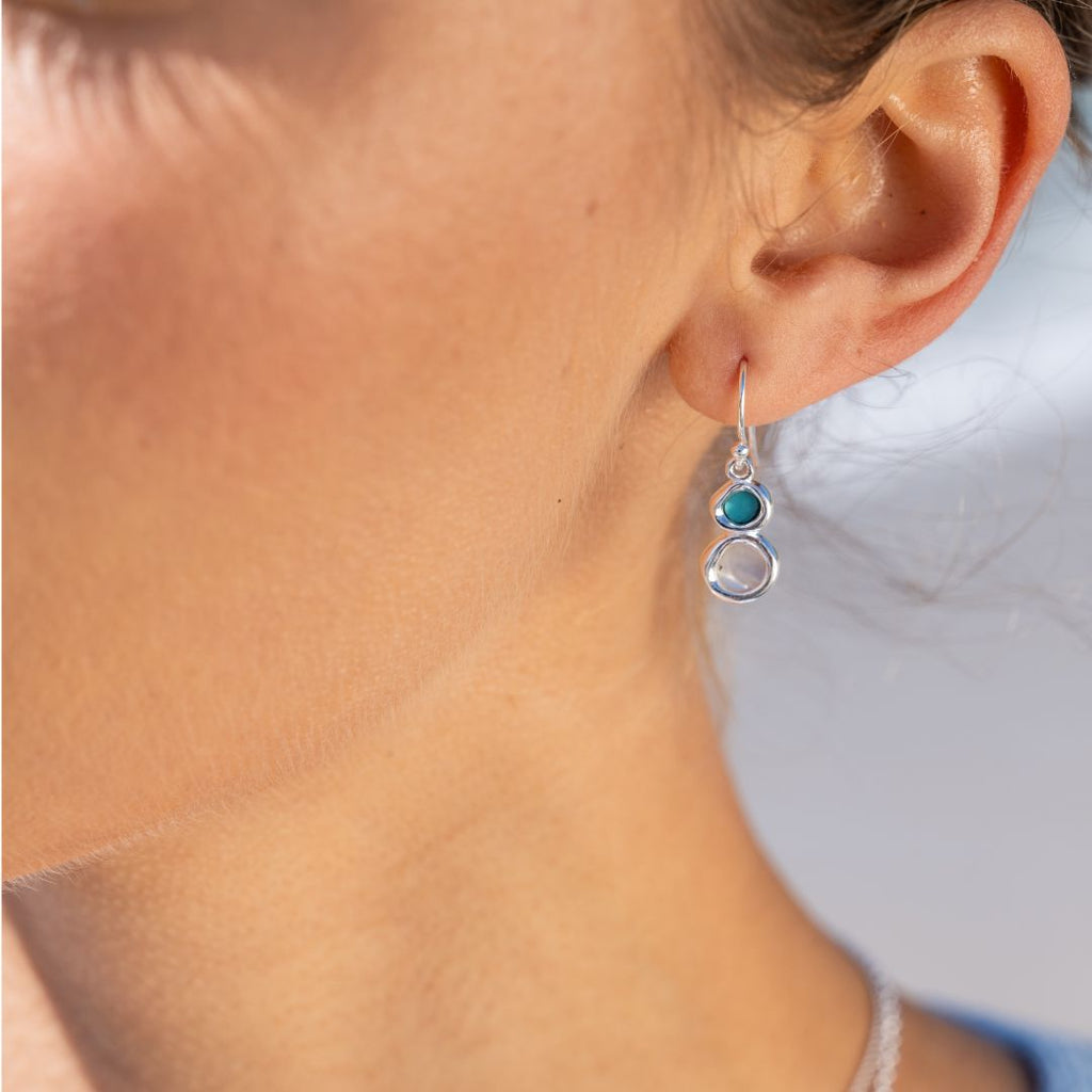 Close-up of a person wearing a silver earring with turquoise and pearl gemstones. 