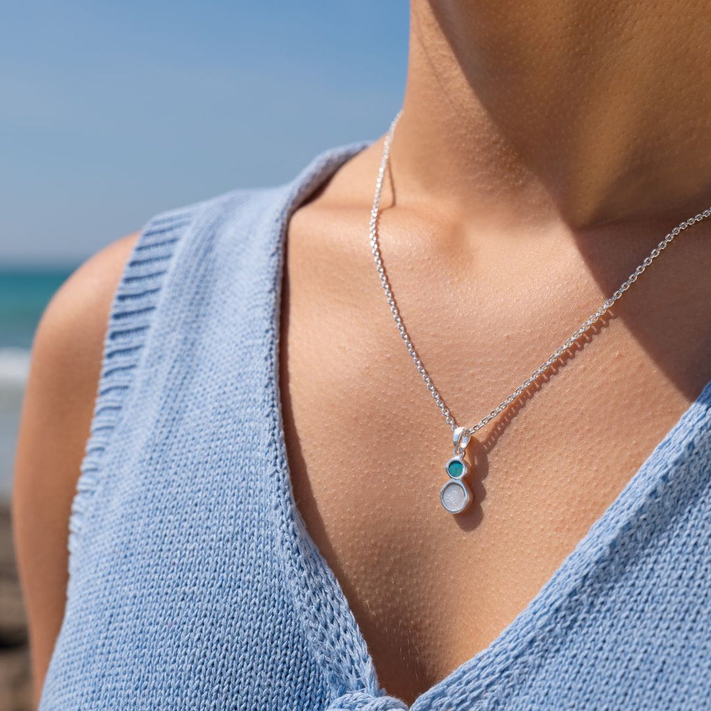 Close-up of a person wearing a silver pendant with turquoise and pearl gemstones. 