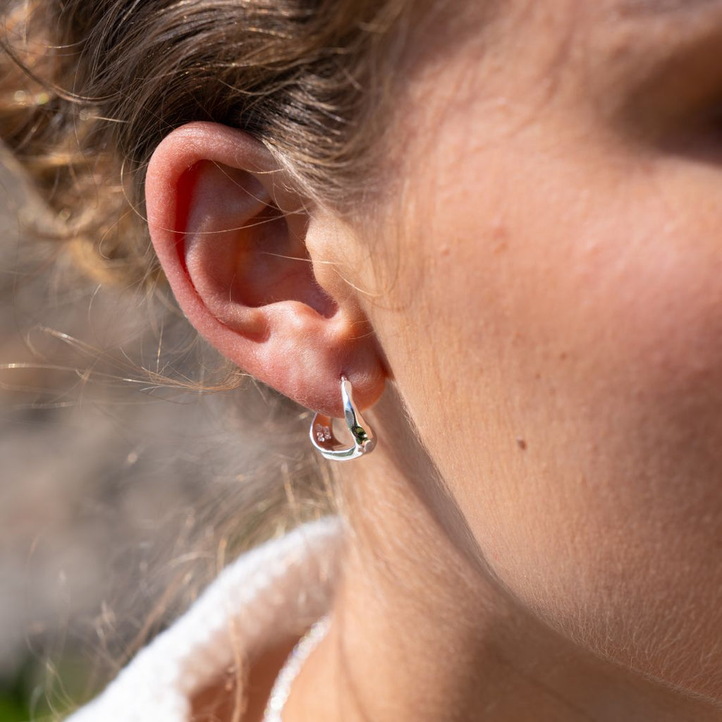 Close-up of an ear wearing a silver hoop earring with a blurred natural background